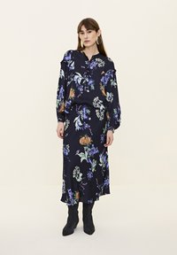 Bluză florală și fustă asortată în albastru închis cu modele purpurii, verzi și portocalii. Țesătura pare netedă; include mâneci bombate și mansete ajustate.