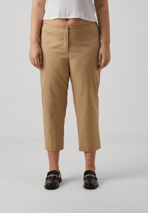 Tan cropped trousers made of smooth fabric, featuring a front button closure and a slim silhouette. Paired with black loafers.