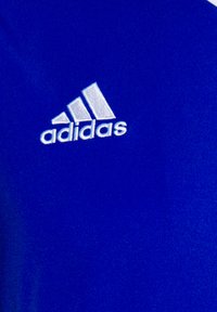 Blå treningsskjorte laget av glatt stoff med en hvit brodert Adidas-logo og tre skrå striper over navnet.