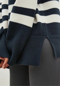 Pull rayé marine et crème, avec poignets et ourlet côtelés, fendu sur le côté en bas, confectionné dans un tissu doux et texturé.