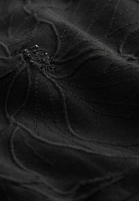 Tissu noir avec broderie florale surélevée, agrémentée de perles noires au centre. Texture lisse avec un éclat subtil.