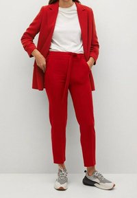 Blazer ajusté rouge et pantalon assorti avec une ceinture nouée, associé à un t-shirt blanc et des baskets grises. Tissu lisse, design ajusté.