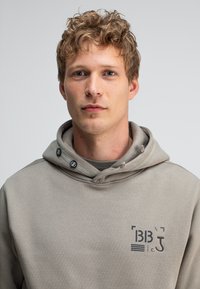 Grijze hoodie met een trekkoord capuchon, voorzien van een bedrukte logo op de borst. Zachte stof met een relaxte pasvorm, minimaal ontwerp en geen patronen.