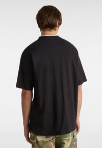 Černé tričko s krátkým rukávem vyrobené z bavlny, s volným střihem a kulatým výstřihem, viděné ze zadní strany se hladkou texturou.