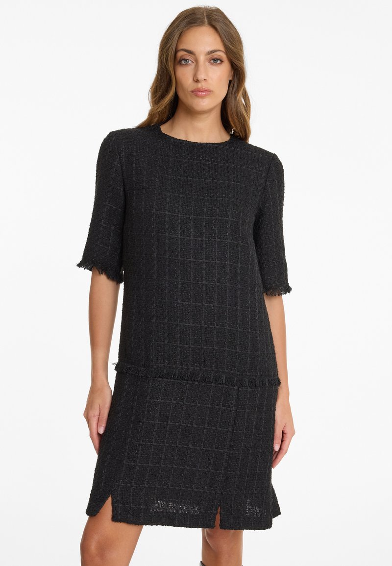 Schwarzes Kleid aus einem strukturierten, gewebten Stoff. Es hat einen geraden Schnitt, kurze Ärmel, Fransen-Details und seitliche Schlitzöffnungen am Saum.