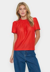 Top corto rosso a maniche corte con scollo arricciato, motivo a diamante texturizzato e vestibilità rilassata. Abbinato a pantaloni in denim.