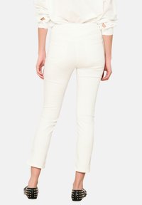 Jeans blancos de corte ajustado, con bolsillos traseros y una longitud ligeramente recortada. Combinados con tacones negros con tachuelas para un contraste.
