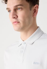 Polo de cor cinza claro feito de algodão suave, com um colarinho texturizado, pala de três botões e logotipo bordado "BOSS" no peito.