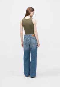 Olivengrønn tanktop med rund hals, kombinert med blå vide jeans med falmet tekstur og en merkevaremerket brun lærlapp på baksiden.