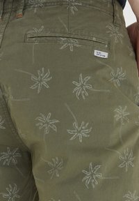 Maslinasto zelene kratke hlače s uzorkom palma, izrađene od lagane tkanine. Imaju stražnji džep i tkanu oznaku s detaljima.
