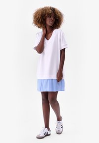 Witte V-hals korte mouwen shirt gecombineerd met een blauw gestreepte geplooide rok en witte sneakers met zwarte accenten. Glad materiaal, casual ontwerp.