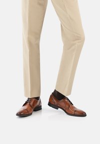 Chaussures habillées en cuir marron avec une finition lisse, design à embout carré et fermeture à lacets classique, assorties à un pantalon beige sur mesure.