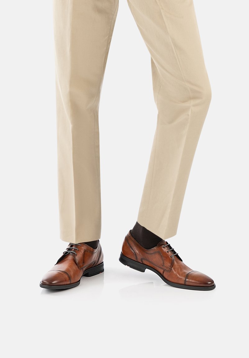 Chaussures habillées en cuir marron avec une finition lisse, design à embout carré et fermeture à lacets classique, assorties à un pantalon beige sur mesure.