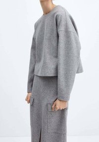 Pull gris court avec épaules tombantes et col rond, associé à une jupe grise assortie avec deux poches appliquées et une fente avant.