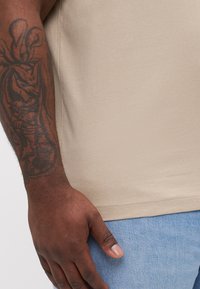 Beige kortermet t-skjorte med en jevn tekstur, tettsittende design og søm-detaljer, sammen med lyseblå denimjeans.