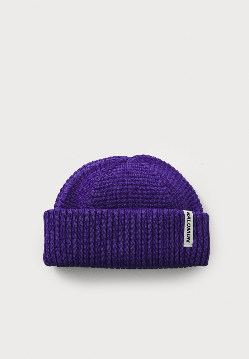 Paarse gebreide beanie met een ribbeltextuur en opvouwbare rand. Heeft een klein wit label met "SALOMON" merk op de zijkant.