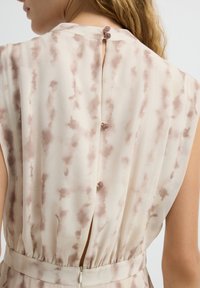 Detalle trasero de un vestido con una tela de color beige claro con patrones en acuarela marrones, cierre de botones y cintura elástica.