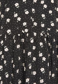 Svart klänning i tyg med vitt blommönster och små vita prickar. Har en samlad midja, mjuk textur och en flödande design.