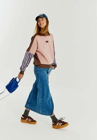 Preširoký ružový a hnedý sveter s pruhovanými rukávmi, doplnený dlhou denimovou sukňou, hnedými teniskami a modrou kabelkou.