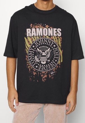 Zwarte katoenen T-shirt met een ronde graphic met het woord "RAMONES," een adelaarsontwerp en grunge-stijl meerkleurige accenten.