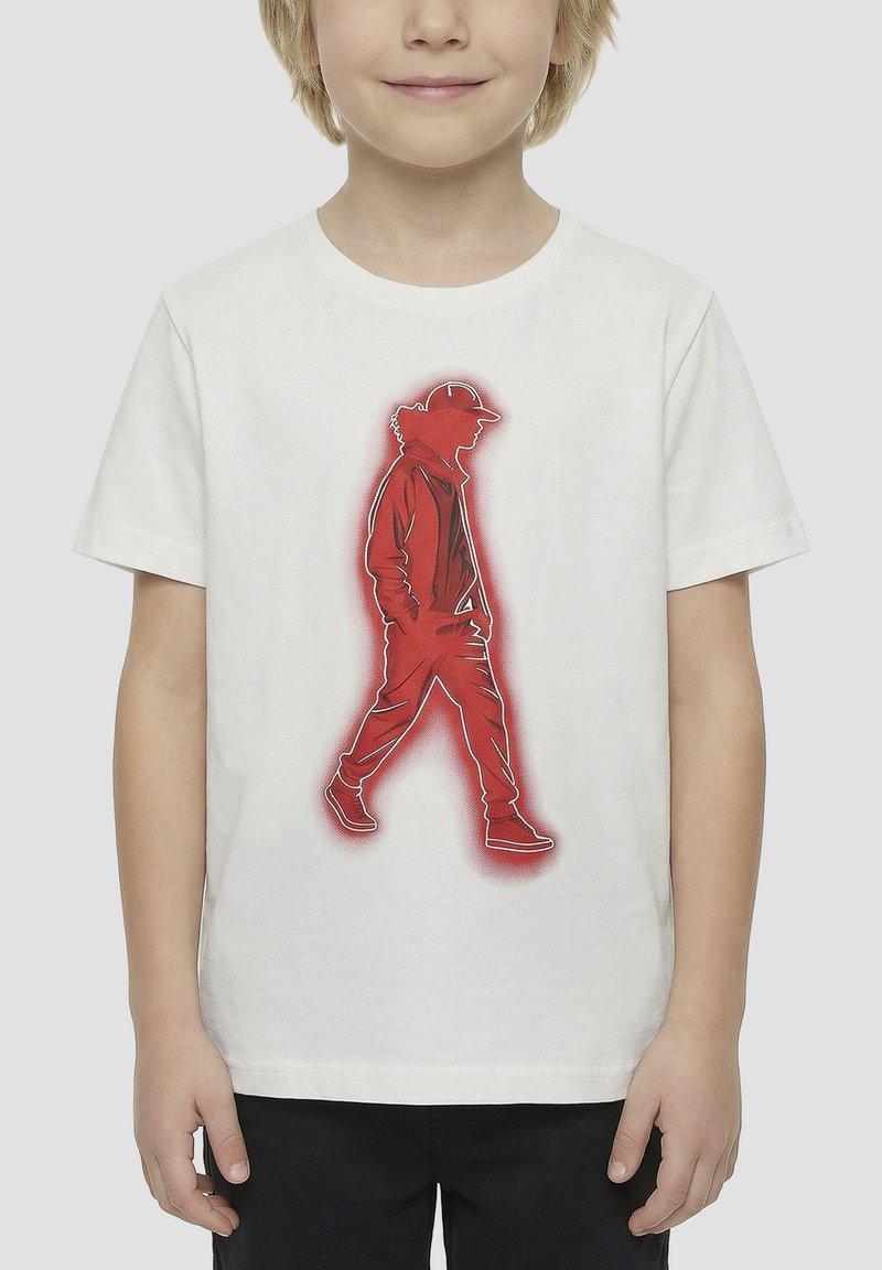 Enfant portant un t-shirt blanc avec la silhouette rouge d'une personne marchant, coiffée d'une casquette et vêtue de façon décontractée, imprimée sur le devant.