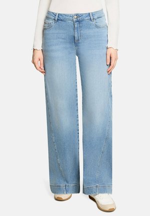 Light blue wide-leg jeans worn with white sneakers and a white long-sleeve top, shown from waist to feet.