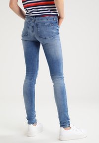 Jeans ajustados de mezclilla azul claro, con una textura descolorida, bolsillos traseros estándar y combinados con zapatillas blancas.