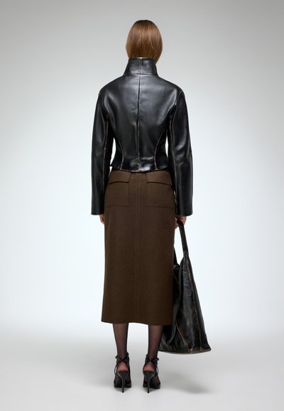 Chaqueta de cuero negra con collar alto, falda de lana marrón y bolso negro. Materiales texturizados, diseño ajustado y detalles visibles de costura en la parte trasera.