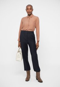 Long-sleeve light brown shirt with a collar, paired with dark navy loose-fitting trousers. Accessorized with a small white handbag and brown ankle boots.