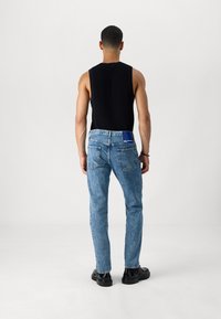 Blue denim jeans with a slim fit, paired with a black sleeveless top. Features five pockets and a visible brand label at the back.