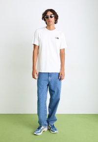 Tricou alb din bumbac cu un mic logo negru, asortat cu pantaloni din denim albaștri deschisi și pantofi sport albaștri.Accesoriile includ ochelari de soare albi.