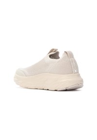 Zapatilla slip-on beige con parte superior de punto texturizado, punta redondeada y suela de goma gruesa con un sutil logo en la parte trasera.