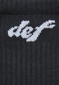 Sorte strikkede sokker med et hvidt logo-design i fed skrift, med et tekstureret mønster og ribbede detaljer i hele stoffet.