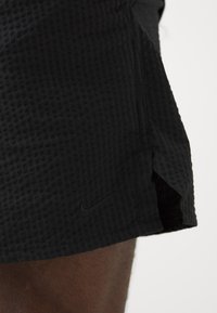 Pantaloni sportivi neri con un motivo a griglia testurizzata, fessure laterali per la mobilità e un piccolo logo Nike nero vicino all'orlo.