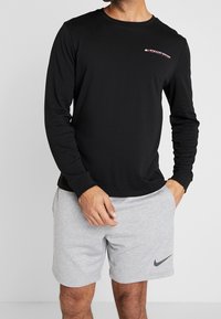 Černé tričko s dlouhými rukávy s logem "TOMMY SPORT" na hrudi, doplněné šedými sportovními šortkami s černým znakem Nike.