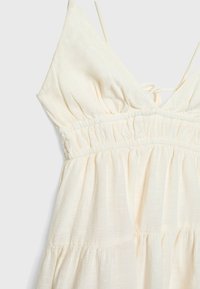 Krémové bezrukávové šaty s tenkými ramienkami, elastickým pásom s nariasením a jemnou, textúrovanou látkou.