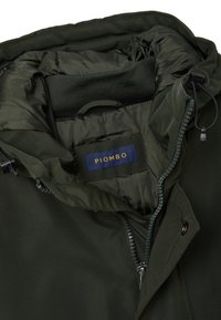 Giacca verde scuro con esterno liscio e leggero, interno imbottito, cappuccio regolabile e etichetta con marchio cucita all'interno. Chiusura con zip.