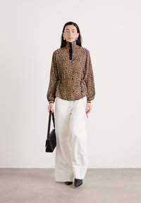 Leopardprint blouse met hoge kraag, lange mouwen en een getailleerde taille, gecombineerd met witte wijde broekspijpen en zwarte hoge laarzen.