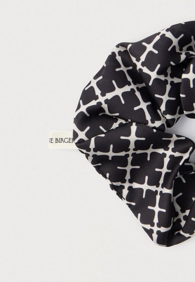 Sort-hvid mønstret scrunchie lavet af glat stof med et geometrisk design og en synlig mærkelabel fastgjort.