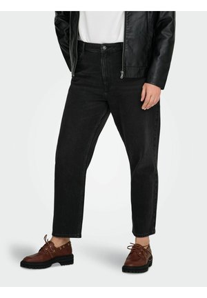 Person iført sorte højtaljede jeans med lige ben, brune snørestøvler, hvid top og sort læderjakke, stående på en ensfarvet hvid baggrund.