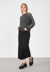 Schwarzer Strickpullover mit strukturierten Ärmeln, kombiniert mit einem hochgeschnittenen schwarzen Jeansrock mit fransenausschnitt und burgunderfarbenen Mary Jane Schuhen.