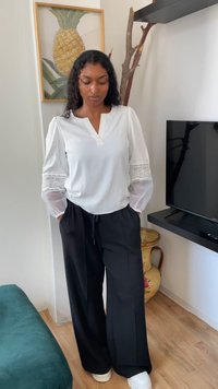 Bluză albă cu detalii din dantelă pe mâneci transparente, asociată cu pantaloni largi negri. Întreaga ținută este completată de adidași albi.