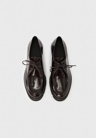 Tamsiai rudi odiniai batai su blizgiu paviršiumi, apvaliu noseliu, pakelta siuvimo linija ir raišteliais su plonais raišteliais.