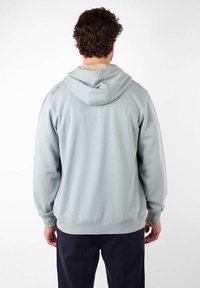 Sweat à capuche gris clair avec une poche kangourou, capuche ajustable et poignets côtelés. Tissu doux et lisse, arborant un petit logo sur l'épaule.