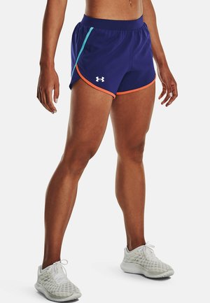 Person iført blå sportsshorts med orange kant og en lyseblå stribe samt hvide løbesko, står mod en helt hvid baggrund.