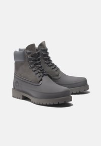 Bottes imperméables grises avec une semelle en caoutchouc, tige en daim et œillets en métal. Présente un col rembourré et un logo sur le côté. Design à lacets.