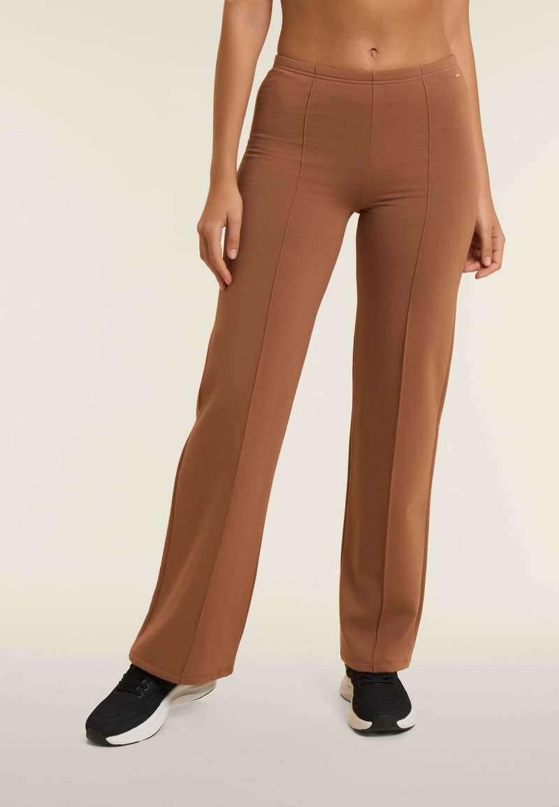 Pantaloni yoga marroni, aderenti, con una texture liscia e dettagli foderati, abbinati a scarpe sportive nere con una parte superiore testurizzata e suola bianca.