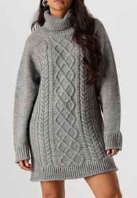 Grijze gebreide coltrui jurk met kabelpatroon, geribbelde mouwen en zoom, en een comfortabele pasvorm die tot halverwege de dij komt.