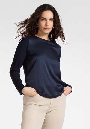 Marineblaues Langarmshirt aus glattem, glänzendem Material. Verfügt über einen runden Halsausschnitt und eine lockere Passform, kombiniert mit hellbeigen Hosen.