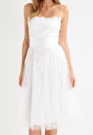 Vestido blanco sin tirantes con un corpiño de encaje, cinturilla de satén y falda de tul en capas con detalles de encaje floral y un dobladillo con borde festoneado.